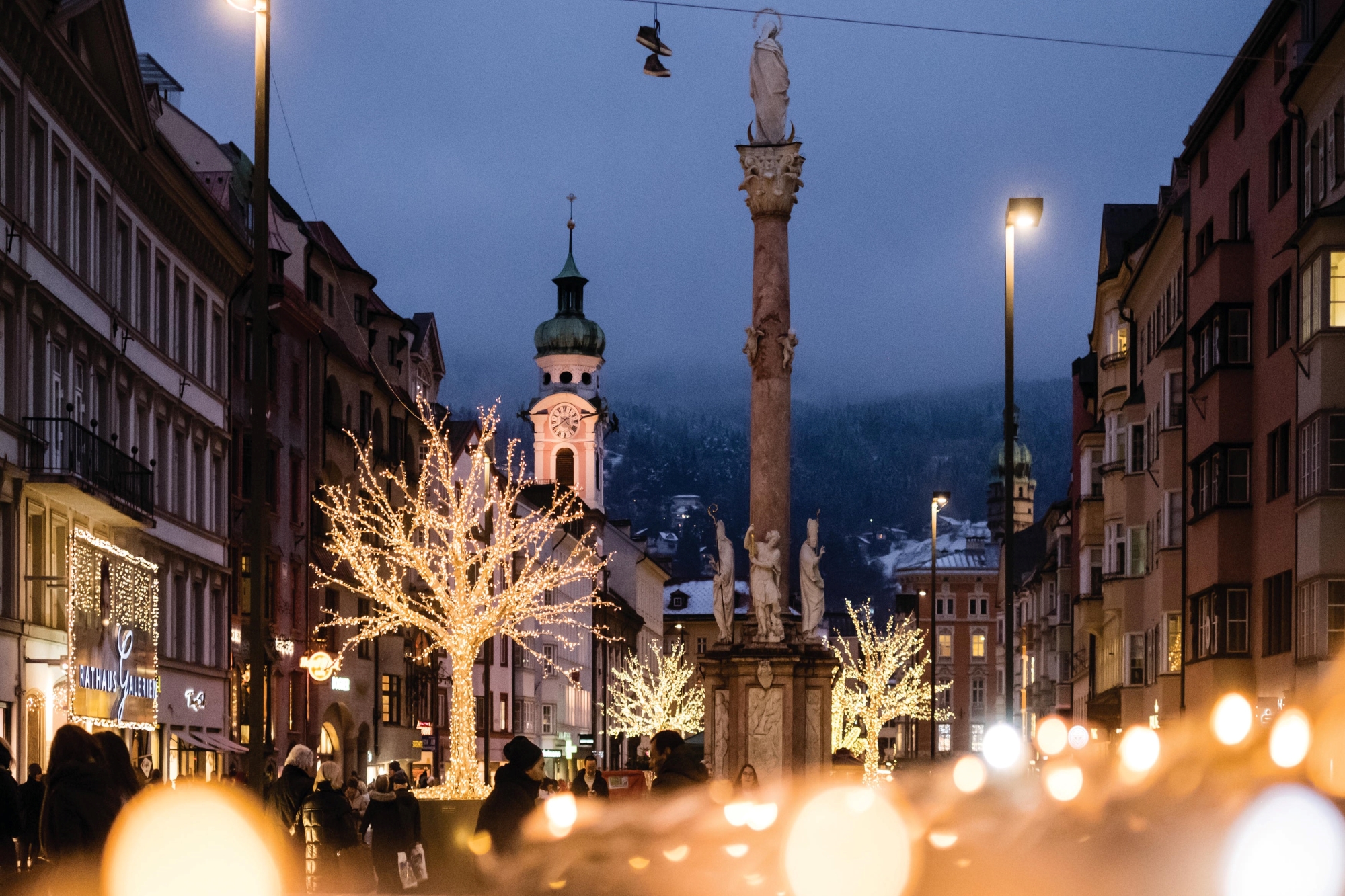 Strada illuminata con alberi decorati ed edifici storici nella luce serale invernale.